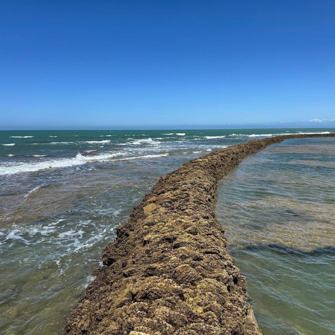 Stone wall of a corral running out into the sea, turquoise water on both sides